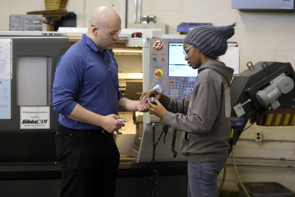 Instructor showing student milled piece of metal