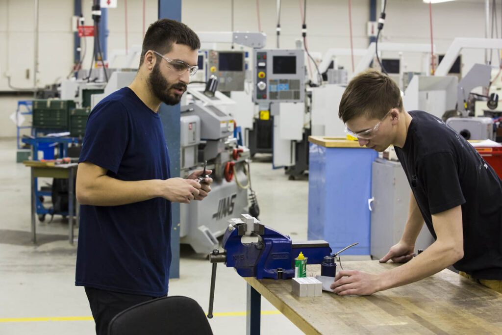 Two people in a CNC lab with one holding a piece of metal