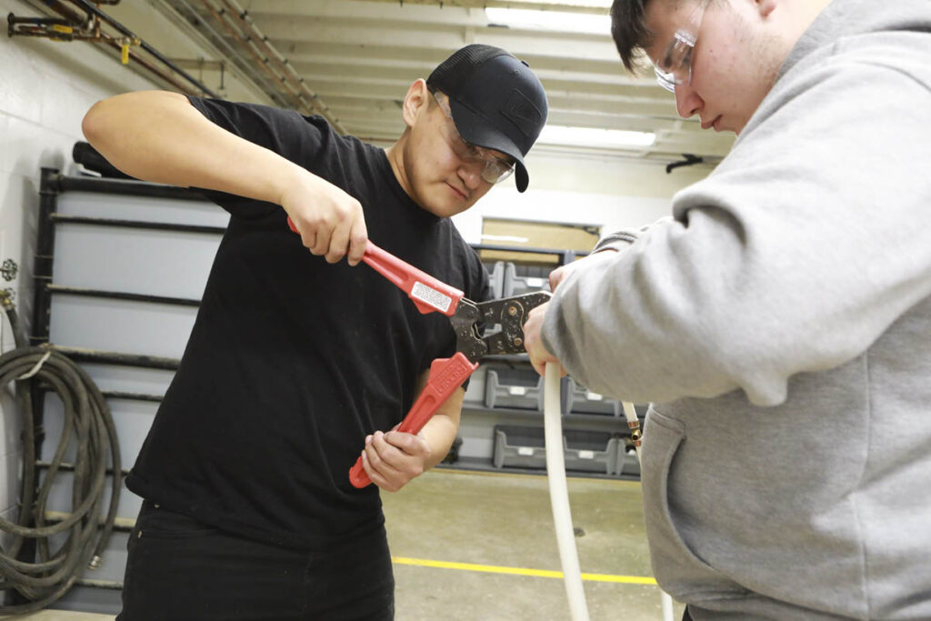 Two students cutting a pipe in a trades shop