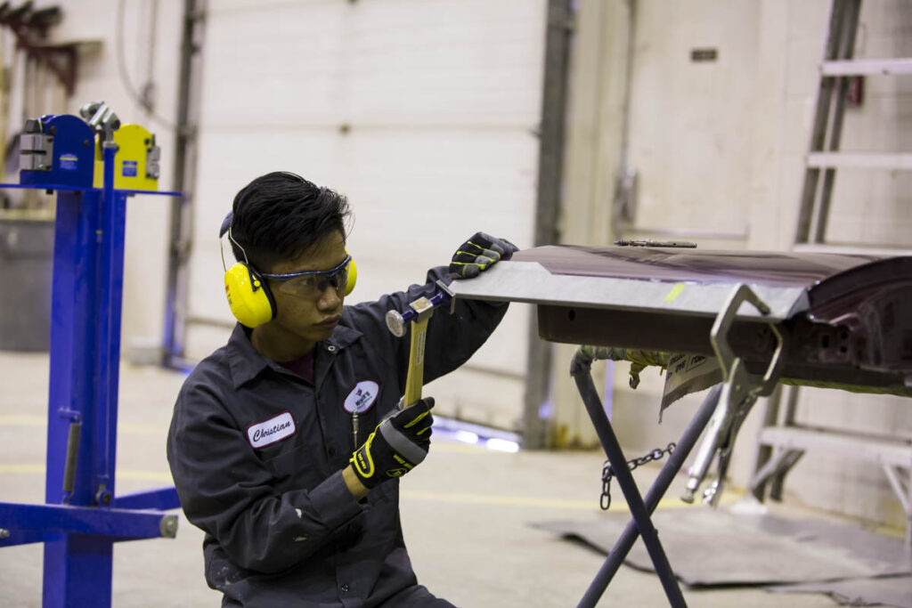 Collision repair student straightening a vehicle panel with a mallet 