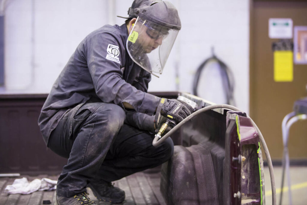 Collision repair student sanding down a vehicle panel while wearing a protective face shield