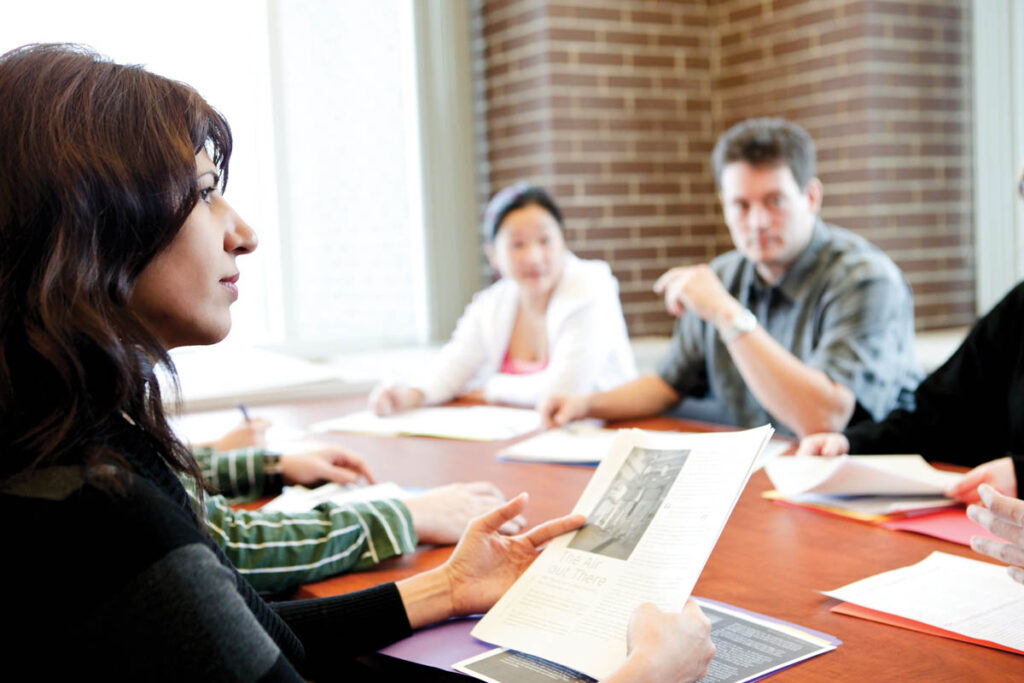 Woman talking to colleagues in a boardroom and holding some notes