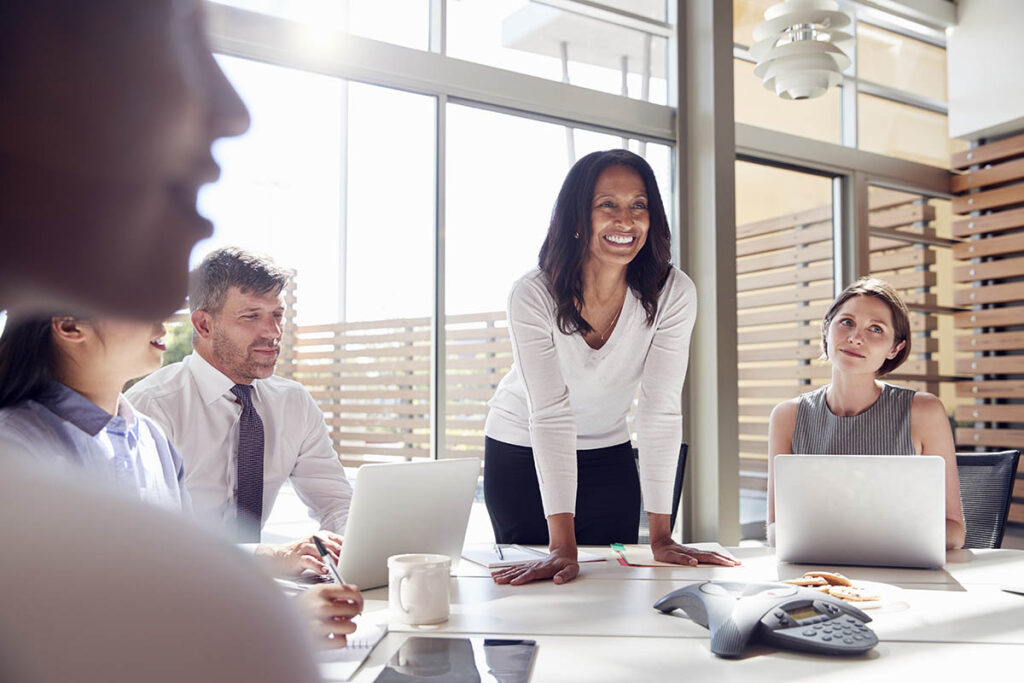 Woman standing at a board room table and talking to her colleagues