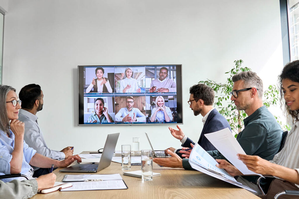 Group of colleagues in a boardroom talking to other colleagues on a video conferencing screen