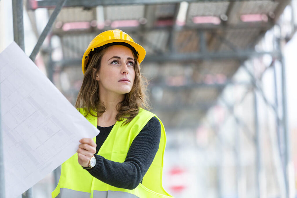 Woman in hard hat and safety vest looking at blueprints