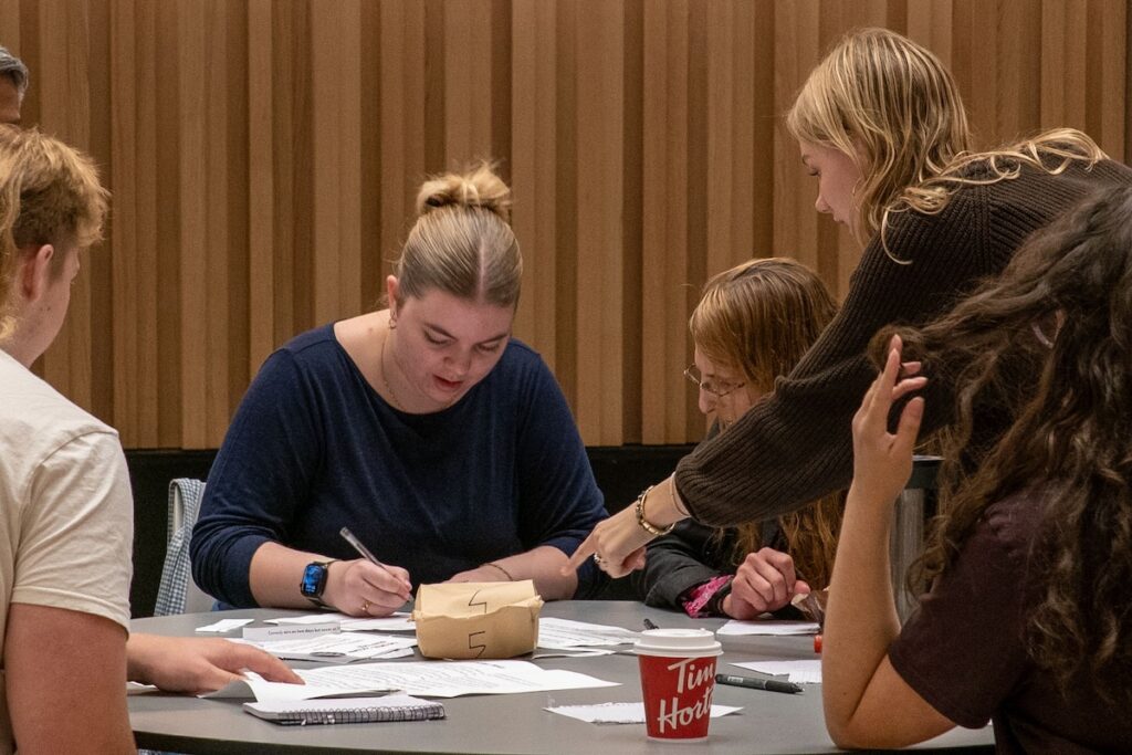 Group of people sitting at a round table and writing something on a paper