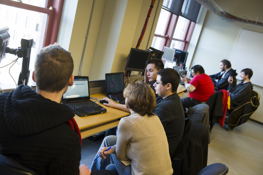 Group of students sitting around a laptop in a classroom