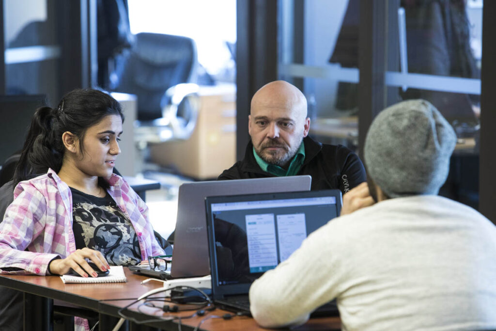 Three students in a classroom looking at their laptops