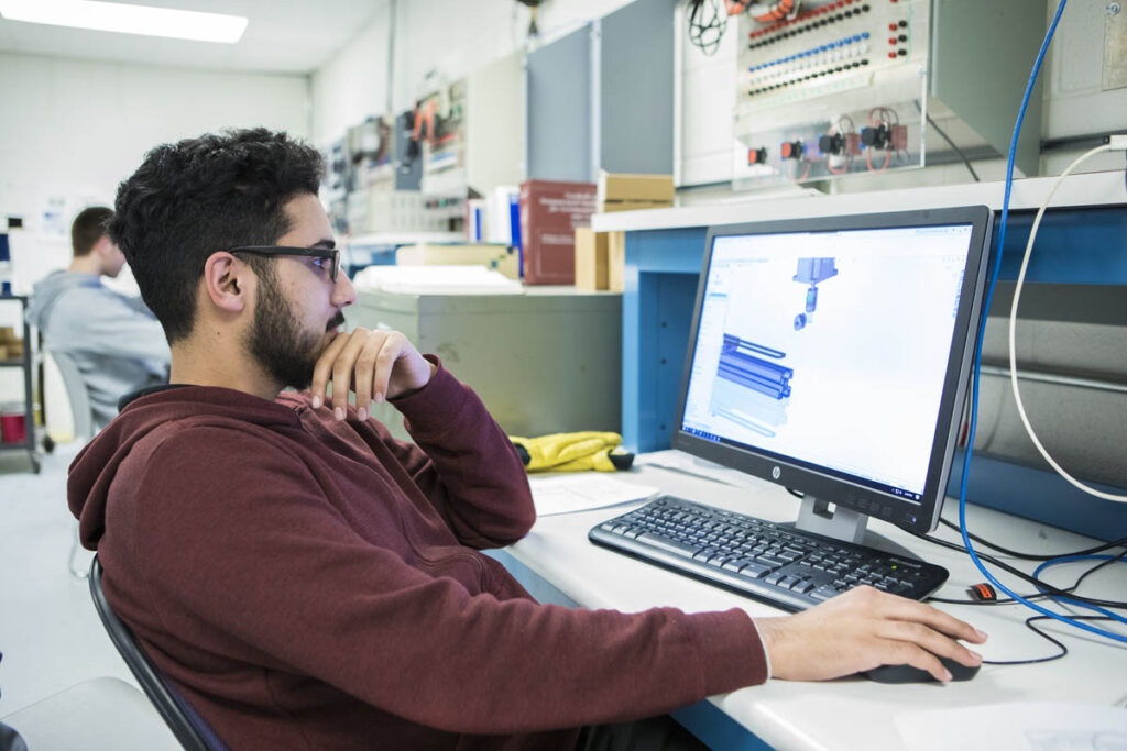 Student sitting in front of a computer screen with drafting software displayed on the monitor