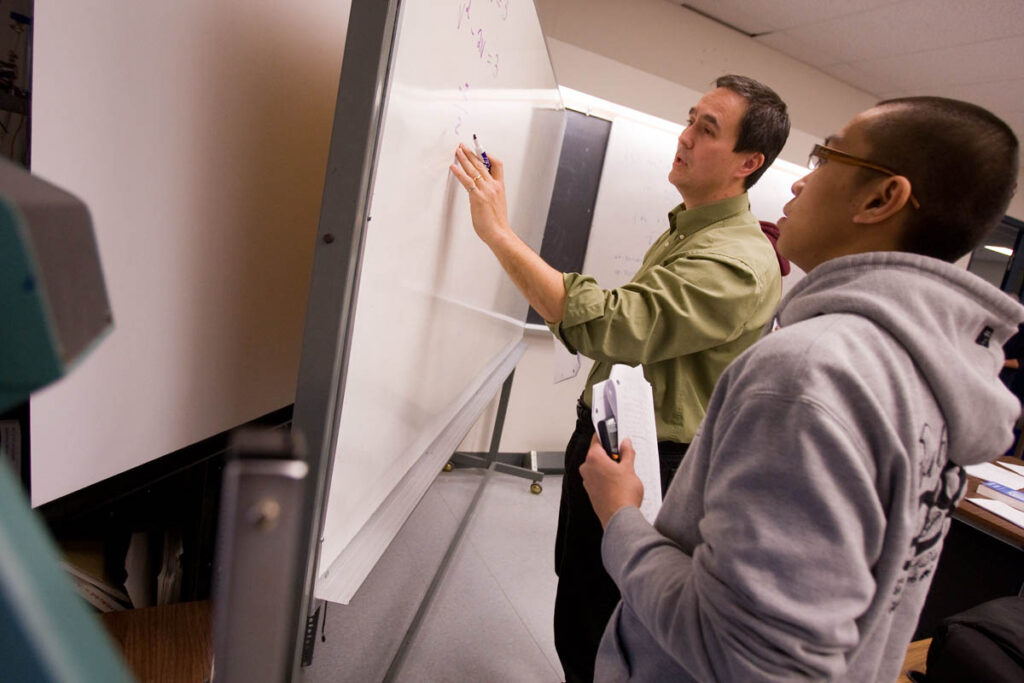 Instructor writing on a whiteboard while a student watches