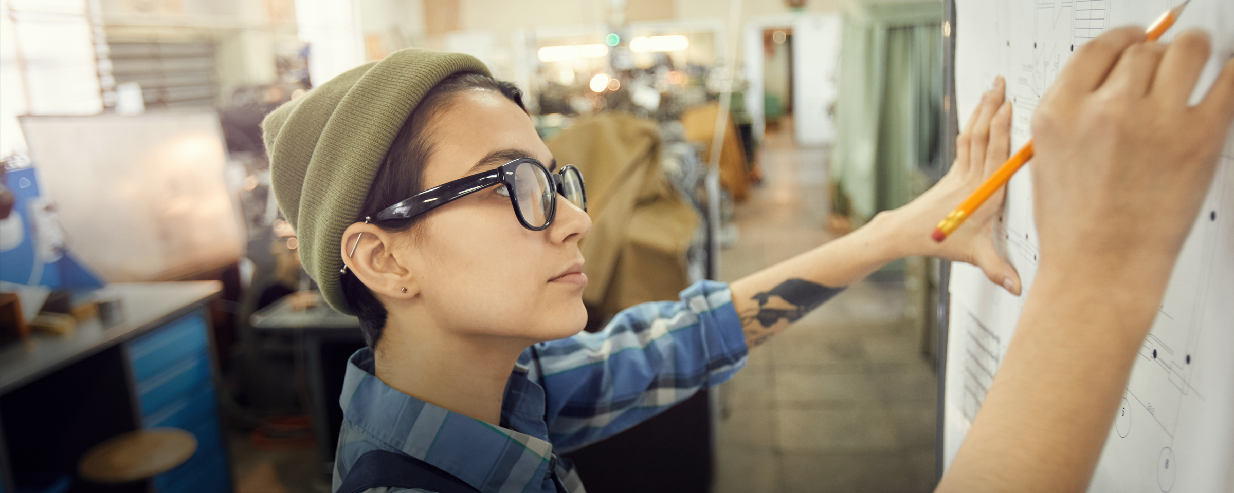 Drafting student drawing on a paper hanging from a wall