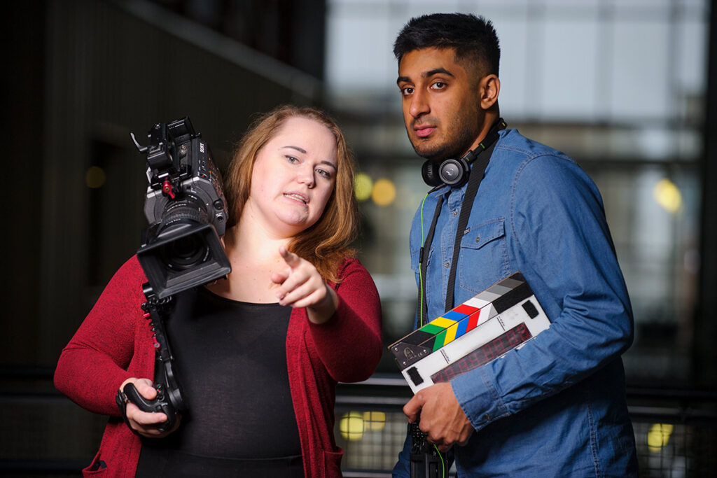 Two film crew workers, one holding a camera, on set