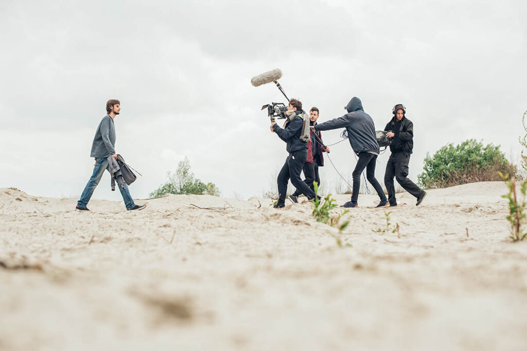 Camera crew filming an actor walking on a beach