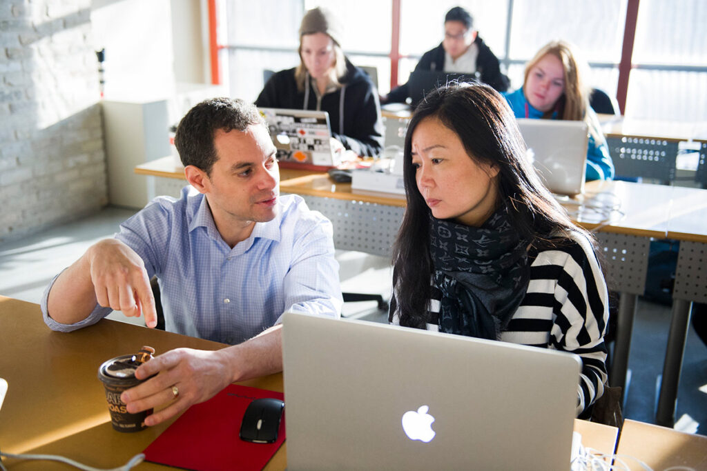 Instructor talking to a student with a laptop in a classroom