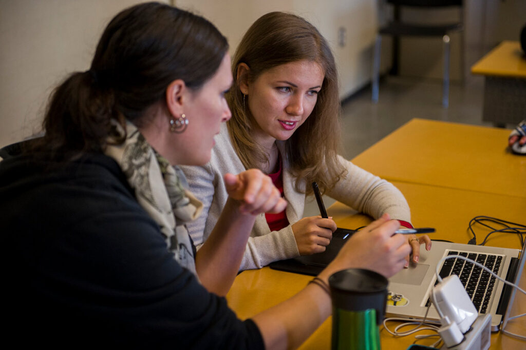 Instructor talking to a student with a laptop in a classroom