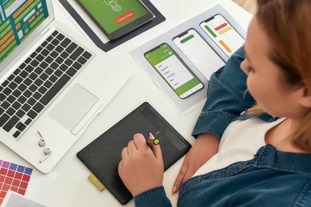 Woman drawing on tablet with wireframes of a mobile app beside her