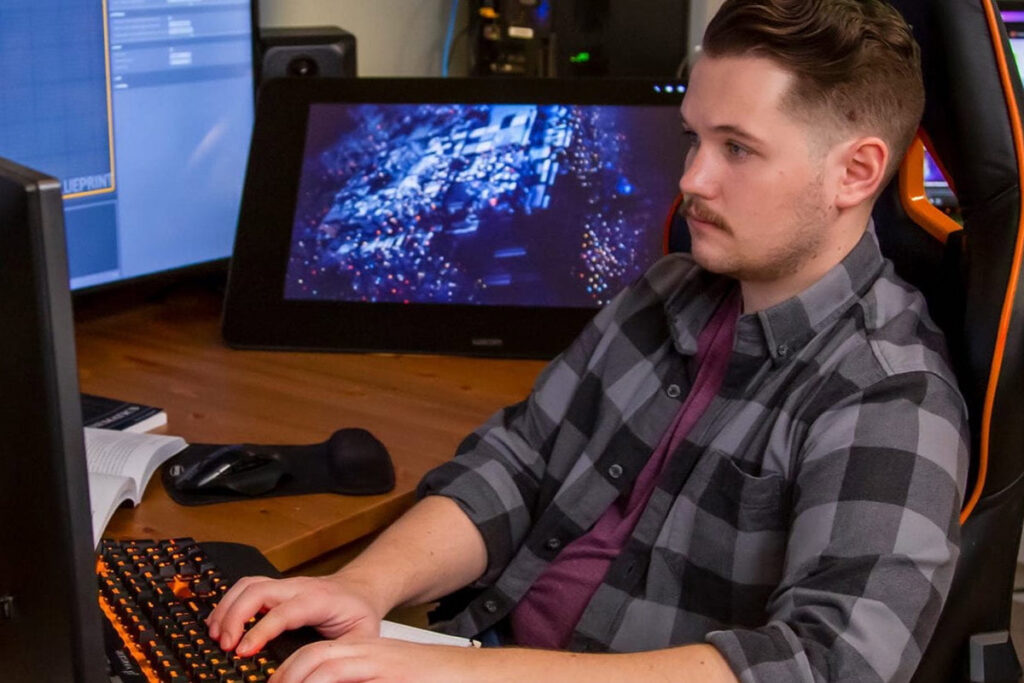 Guy typing on a keyboard and looking at multiple monitors in his home office