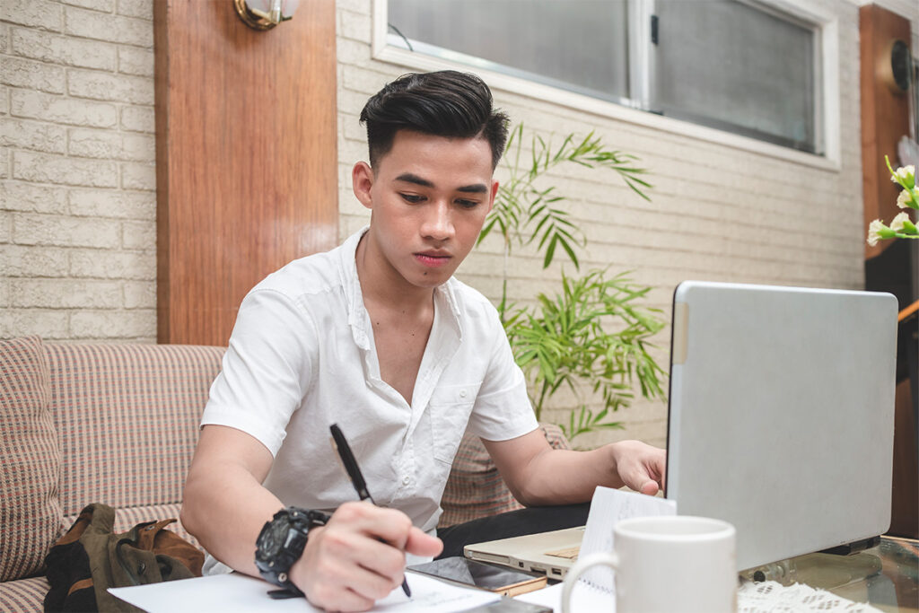 Guy taking notes at table while sitting by his laptop