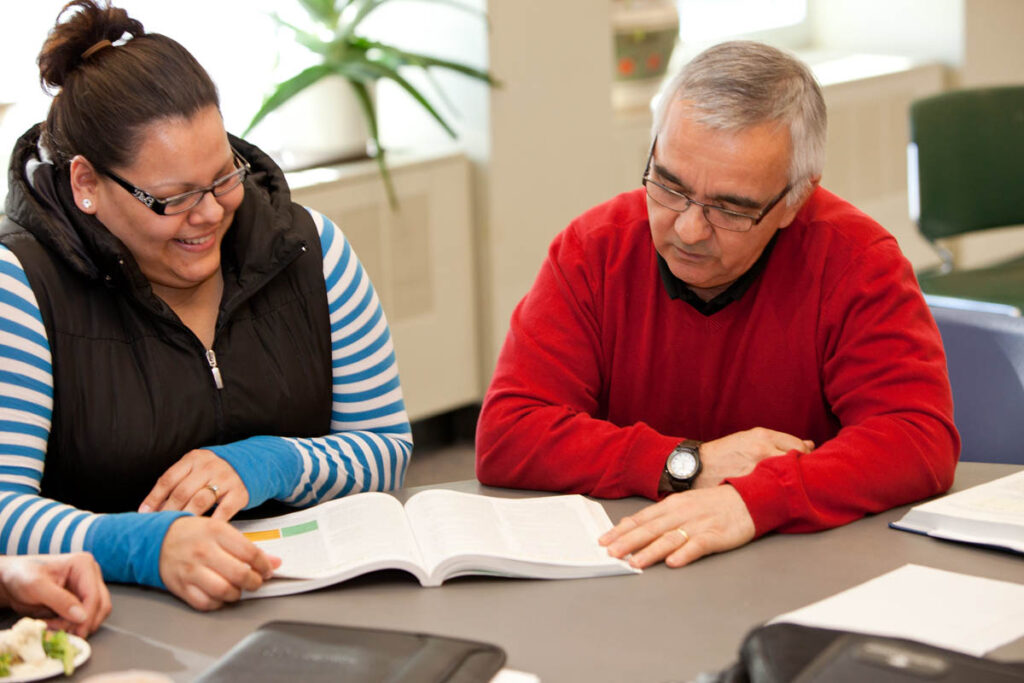 Instructor talking to student in a classroom and looking at a textbook