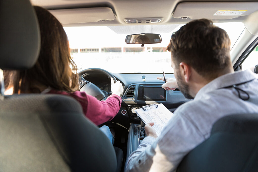 Driving instructor and student sitting inside a car while the instructor takes notes