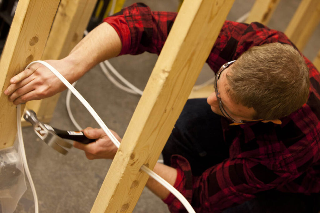 Electrical student in training construction site fastening wire to frame