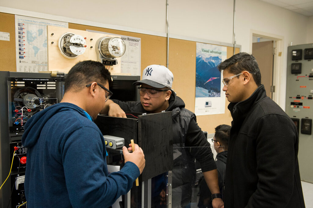 Three students looking inside electronic device in a lab