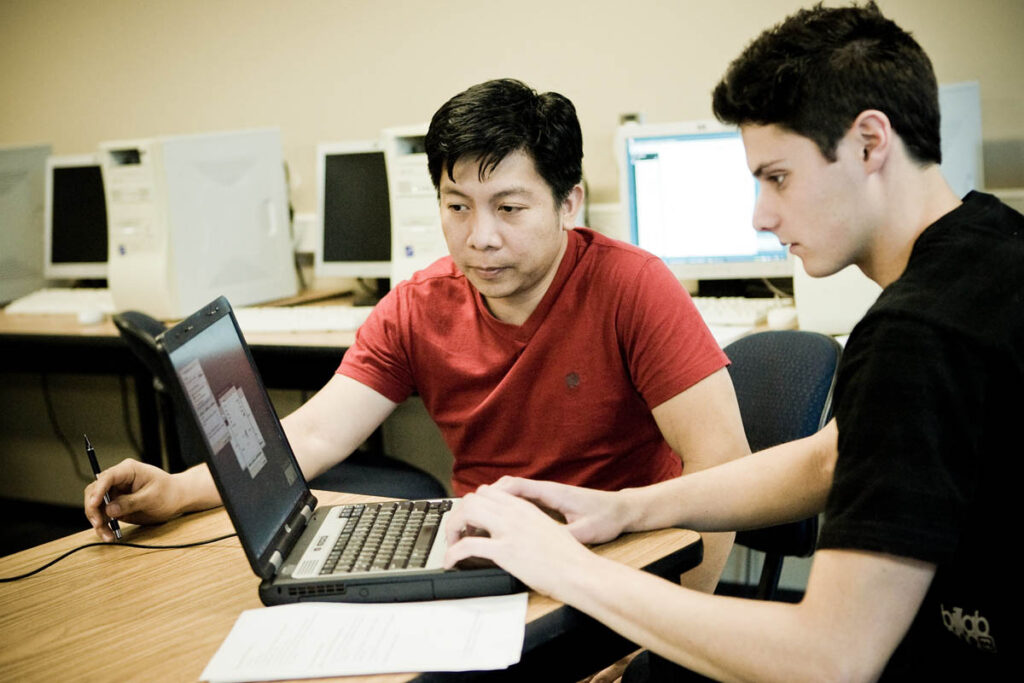Two students working on a laptop in a computer lab