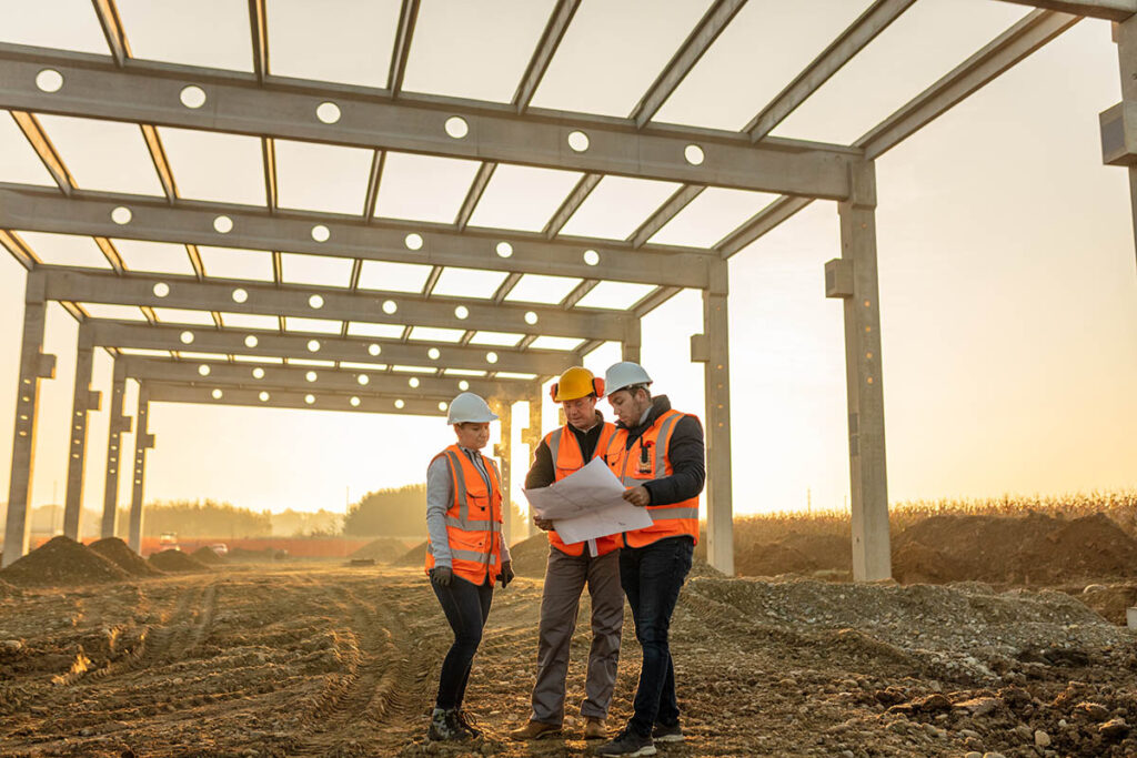 Three people looking at blueprints while underneath the frame of a newly built structure