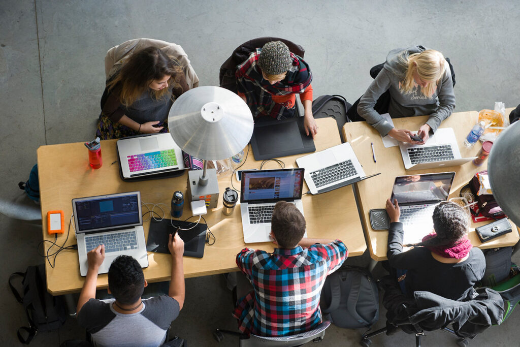 Overhead shot of six students sitting at a table and working on their laptops