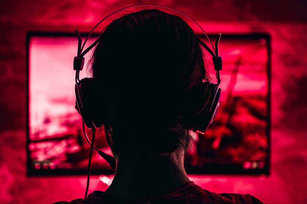 Silhouette of person with large headphones on looking at computer screen