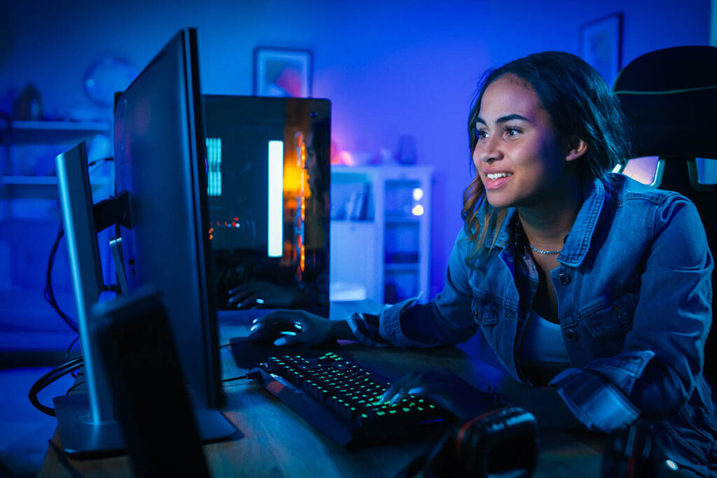 Girl in a dimly lit room working on a computer with dual monitors