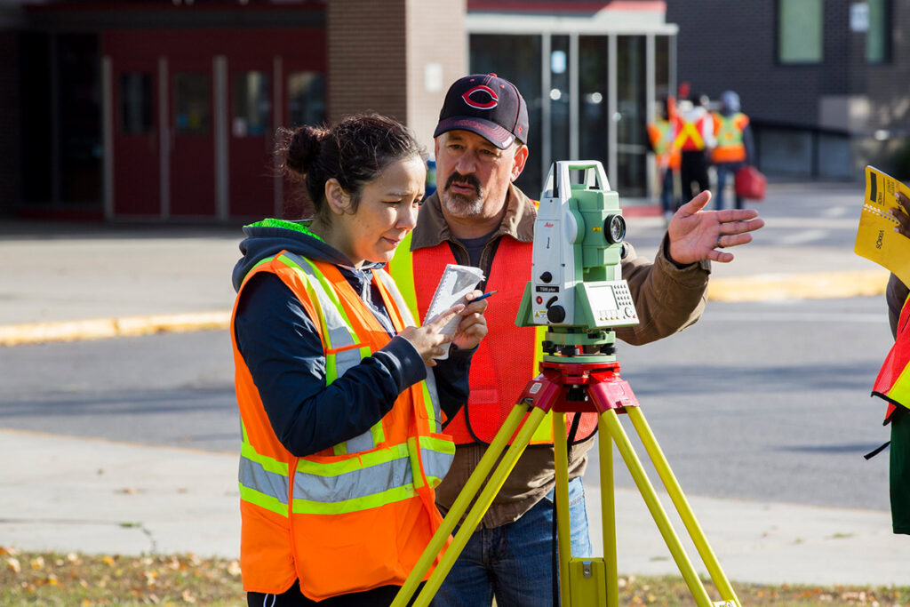 Instructor teaching student how to use surveying equipment outdoors