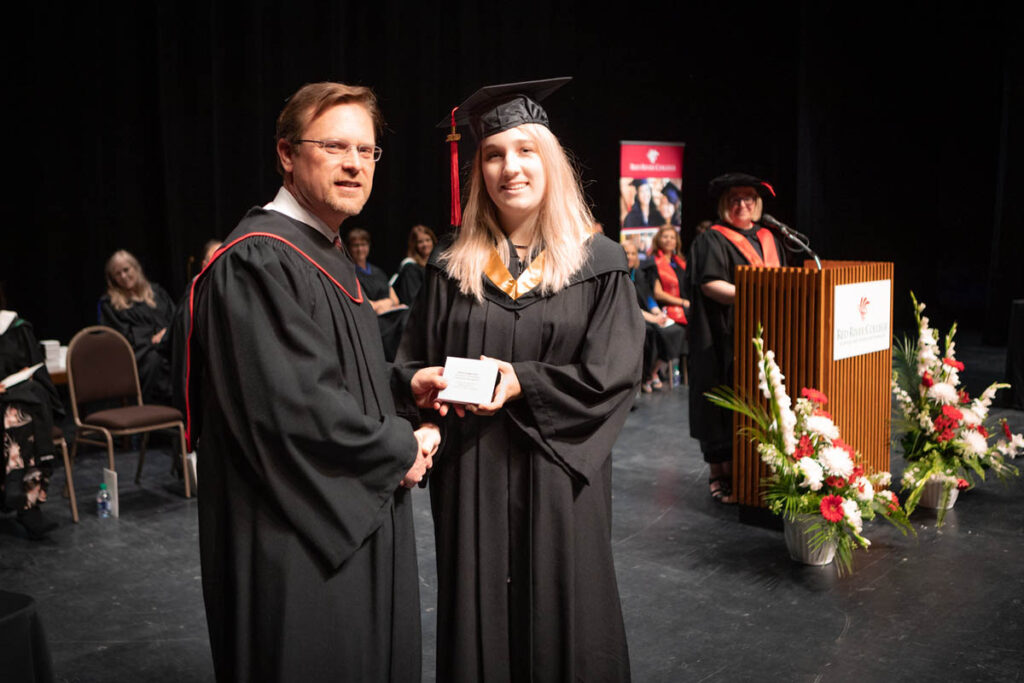 Two people posing at graduation holding a document