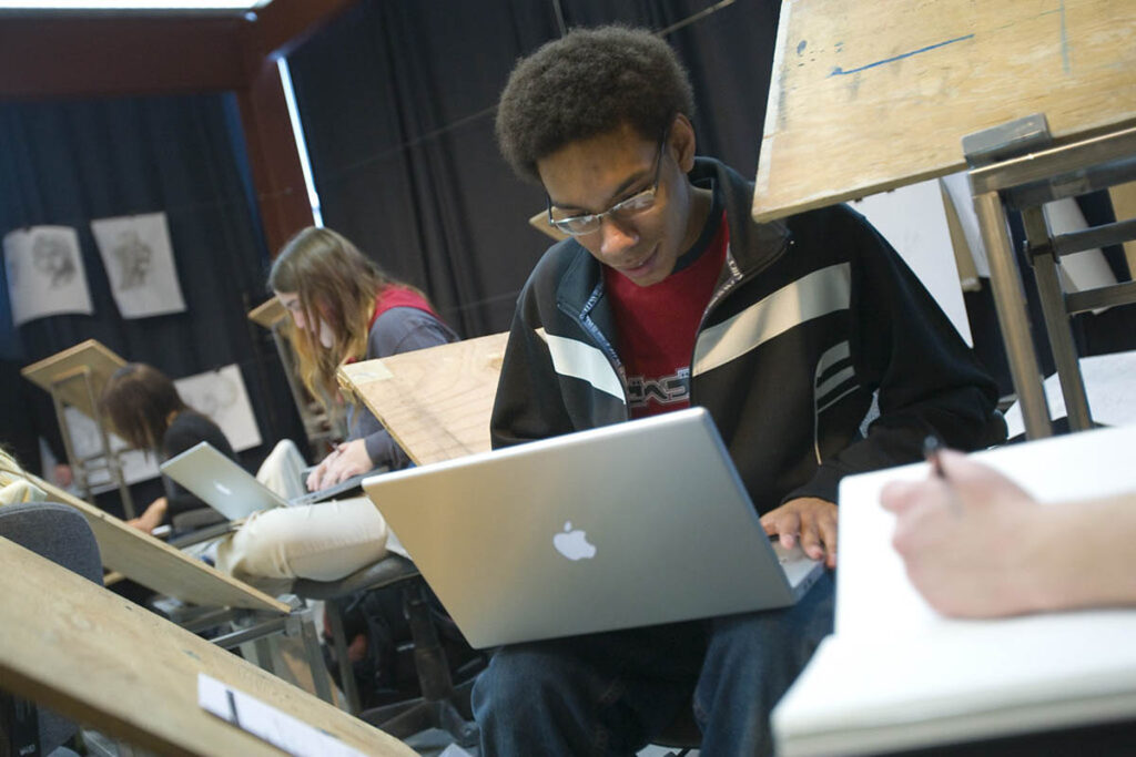 Student sitting in an art class working on a laptop