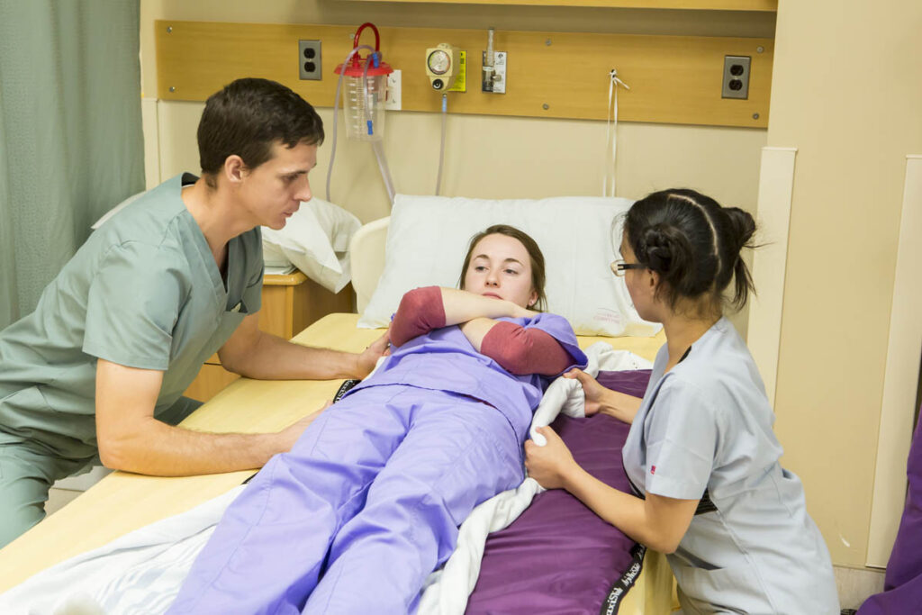 Health care aides assisting patient in hospital bed