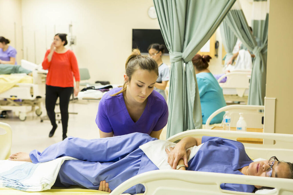 Health care aide student practicing assisting patient in hospital bed