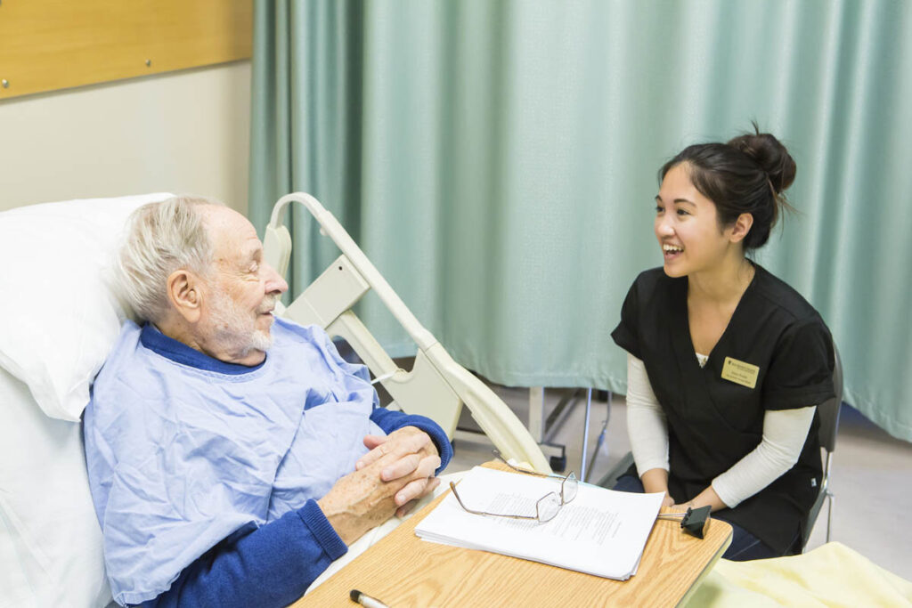 Health care aide talking to patient in hospital bed