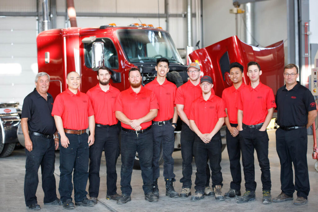 Group of mechanic students standing in front of a semi truck in a shop