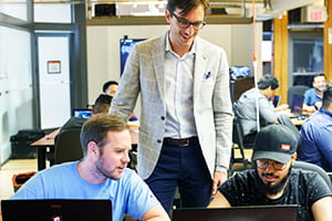 Instructor standing by students with laptops