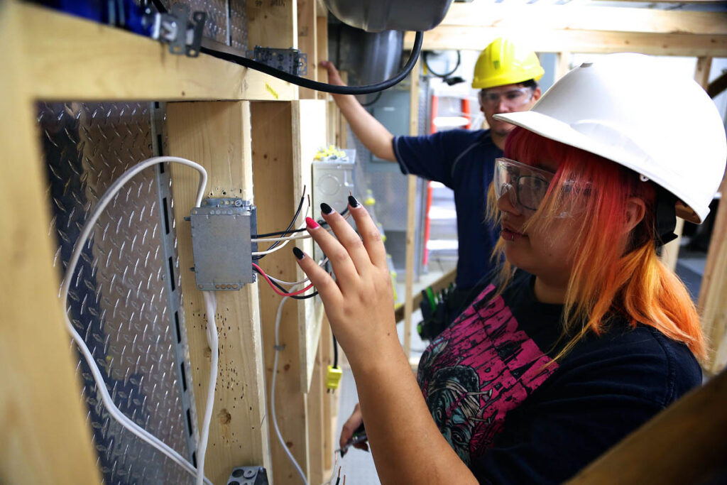 Student wiring switch at simulated construction site while instructor looks on