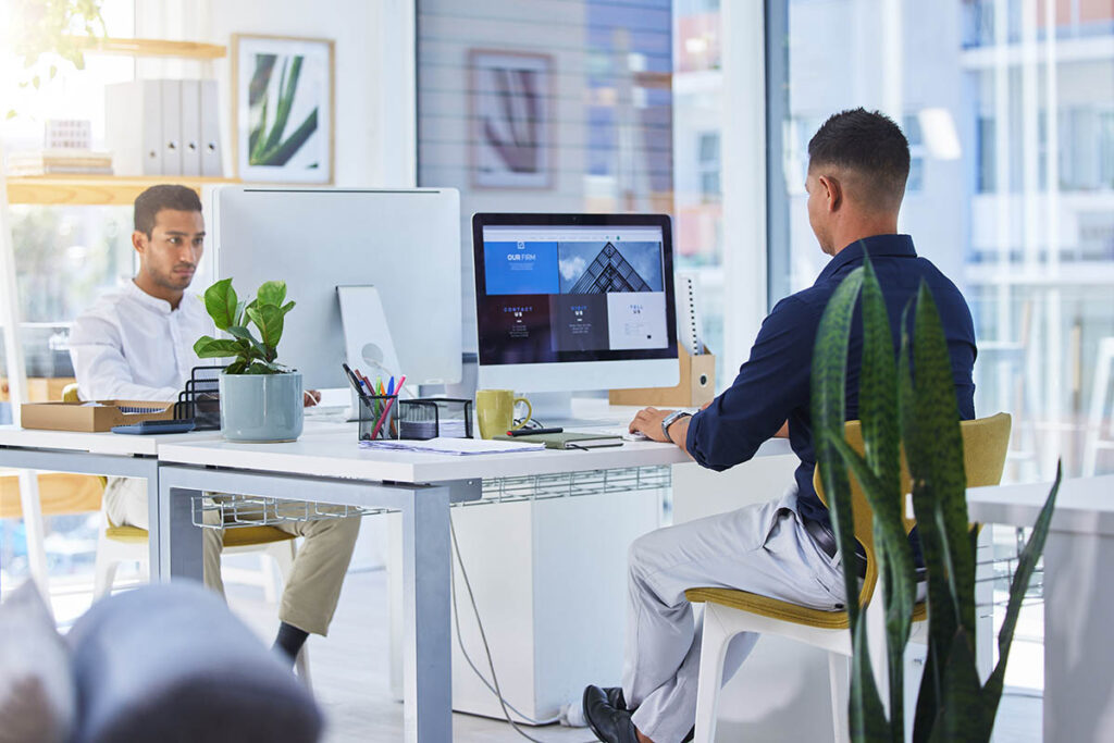 Two people sitting at a desk in an office and working on computers