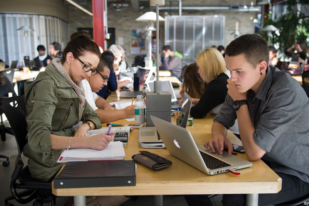 Students working on laptops in an open workspace on campus