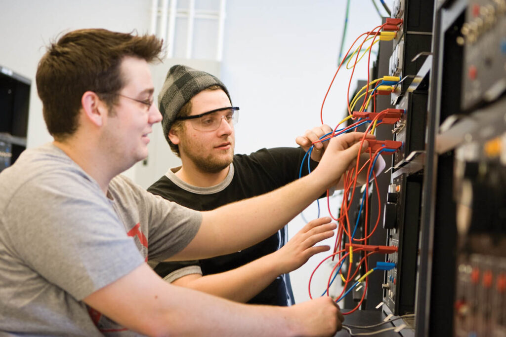 Electrical engineering students plugging cables into device in a lab