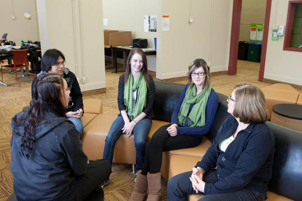 Group of students talking to their instructor in a lounge on campus