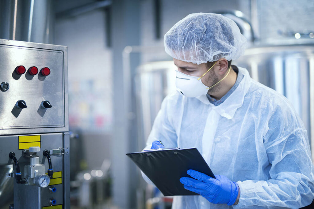 Person wearing protective gear and holding a clipboard in a food manufacturing plant