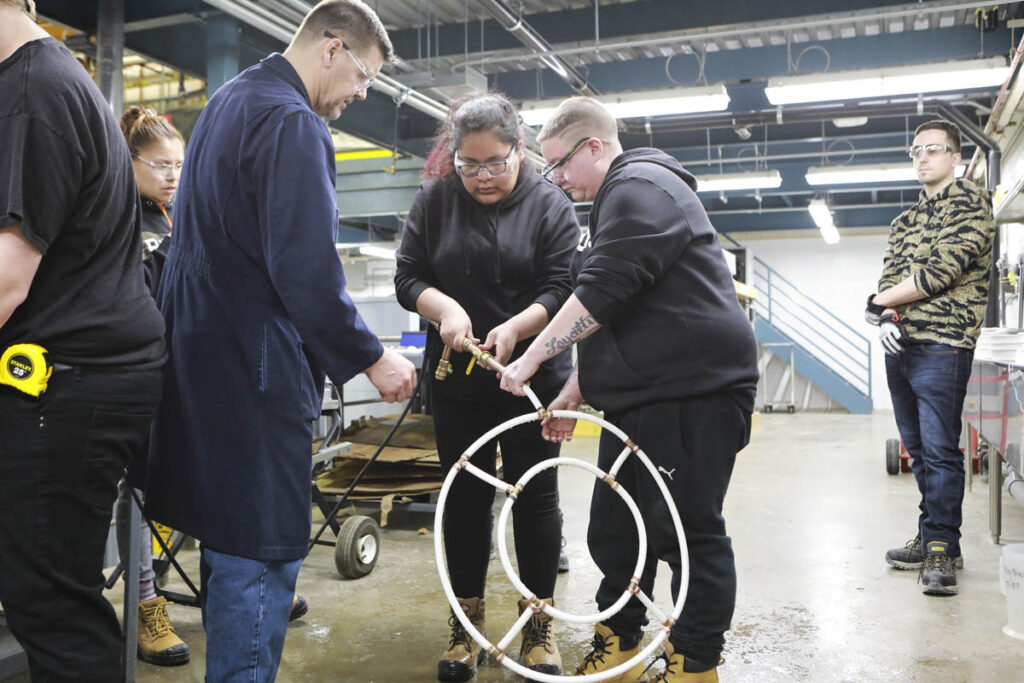 Instructor watching two trades students fit pipes together