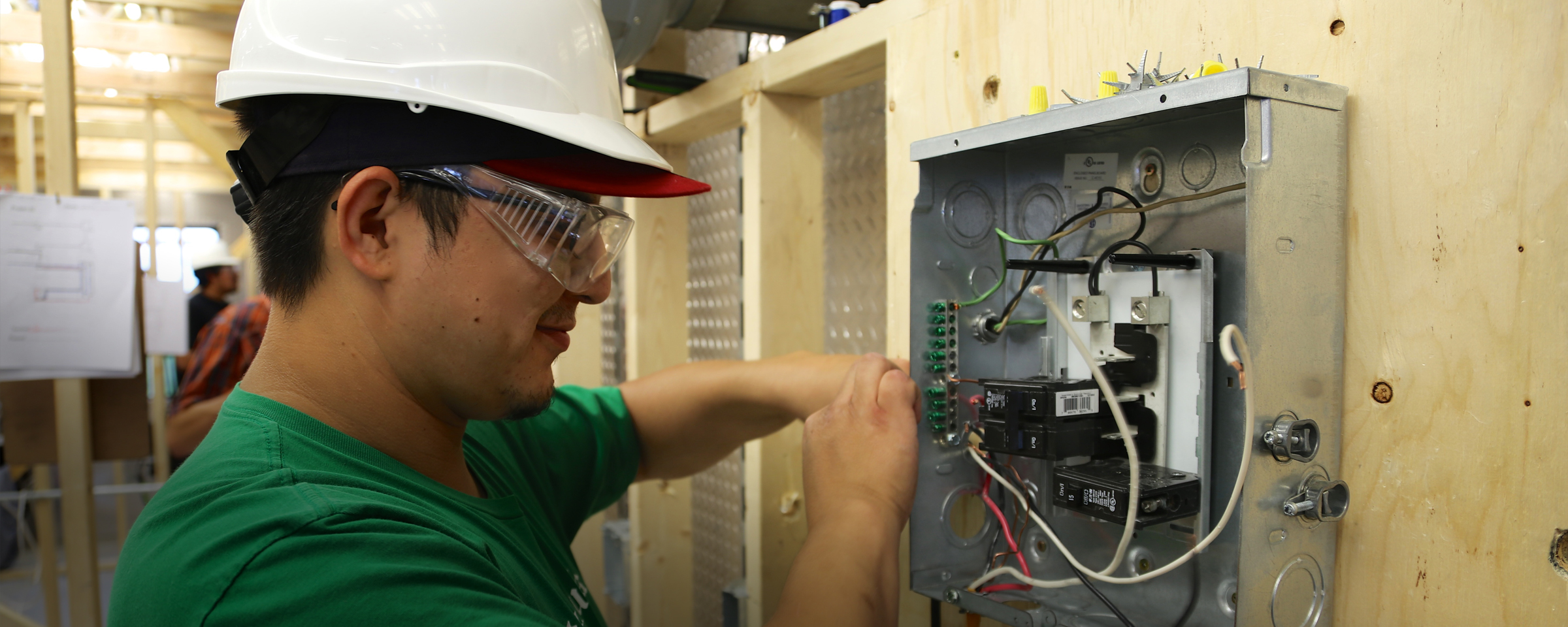 Electrician student wiring a breaker box at a simulated construction site