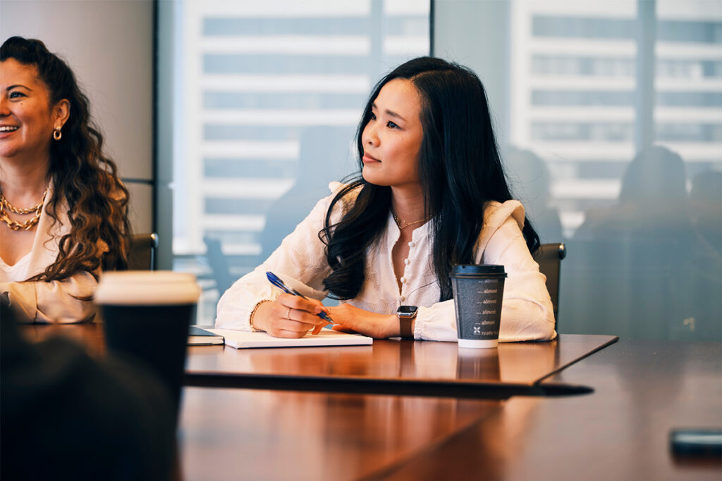 Woman with a pen and notebook listening to a speaker in a meeting room