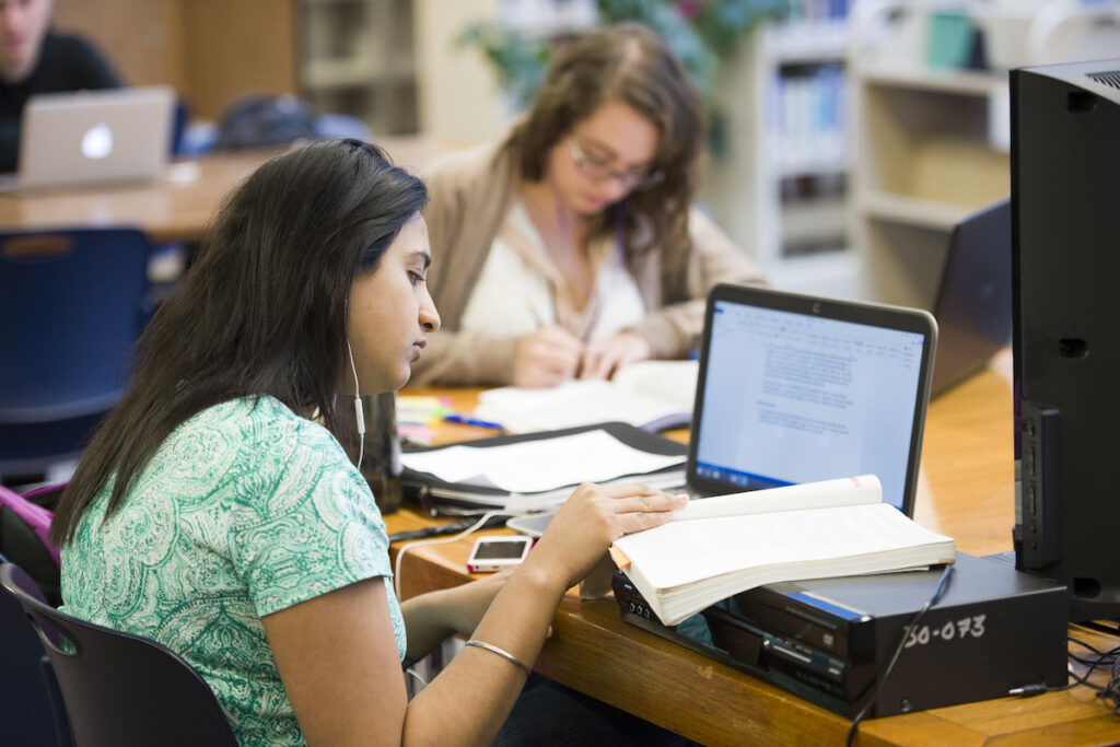 Students reading textbooks and taking notes on laptops