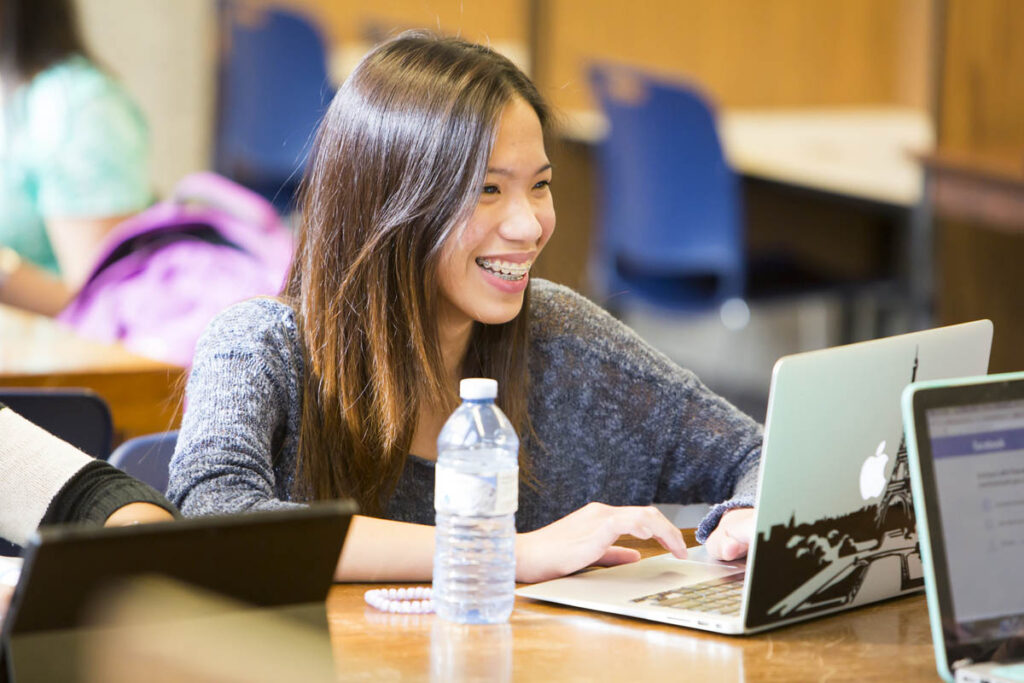 Smiling student working on a laptop in a classroom